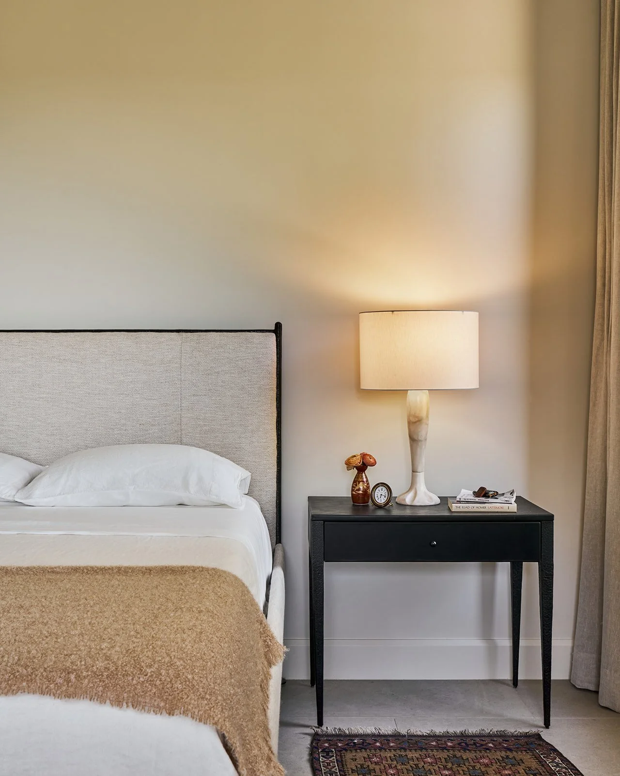 Minimal Austin interior design primary bedroom featuring a Baker McGuire upholstered bed, coordinating nightstand, and vintage alabaster table lamp.