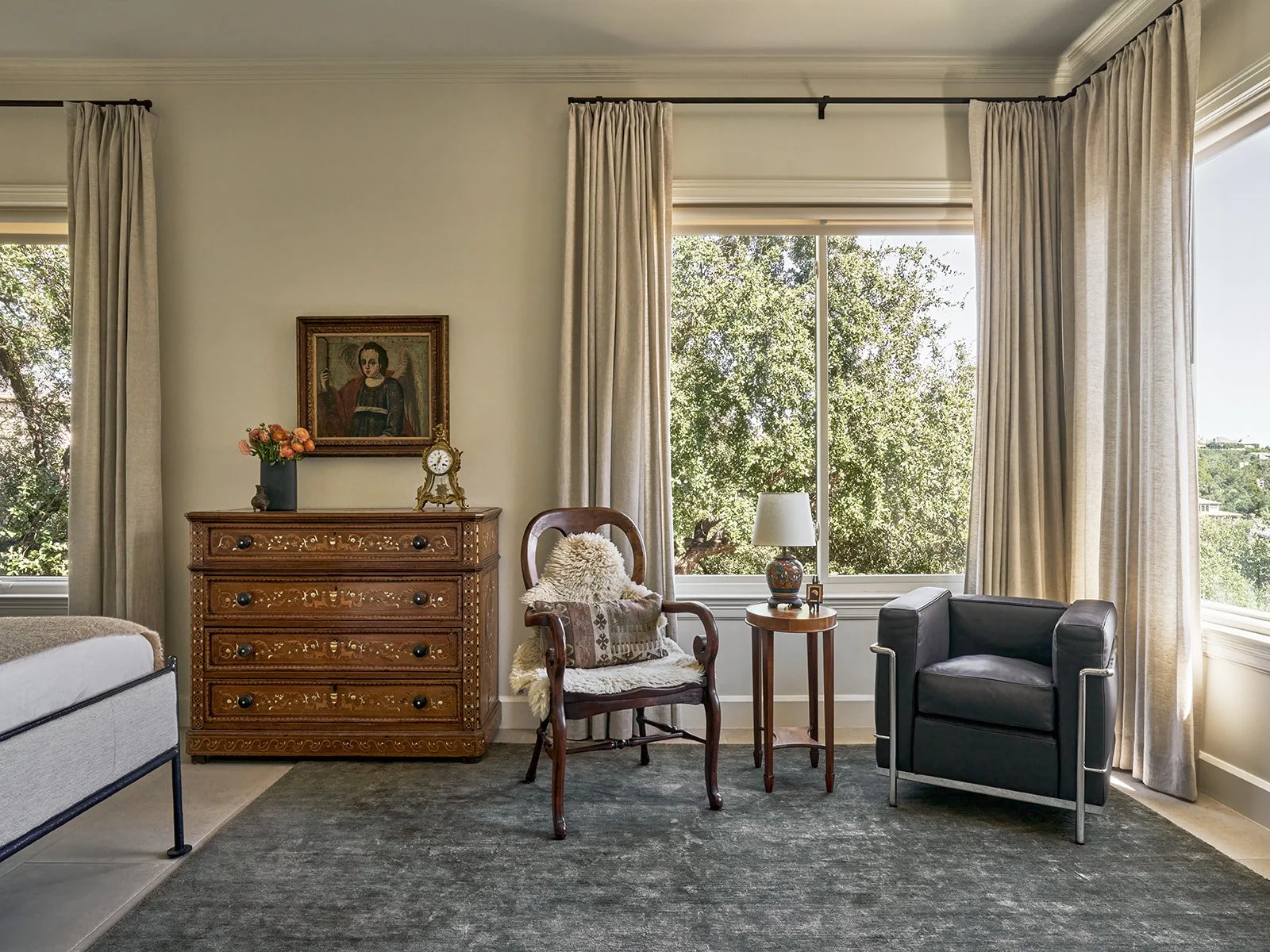 Primary bedroom featuring a solid green linen rug, antique dresser with a vintage Archangel Raphael painting, a classic antique chair, and a Cassina 3 Fauteuil Grand Confort chair.