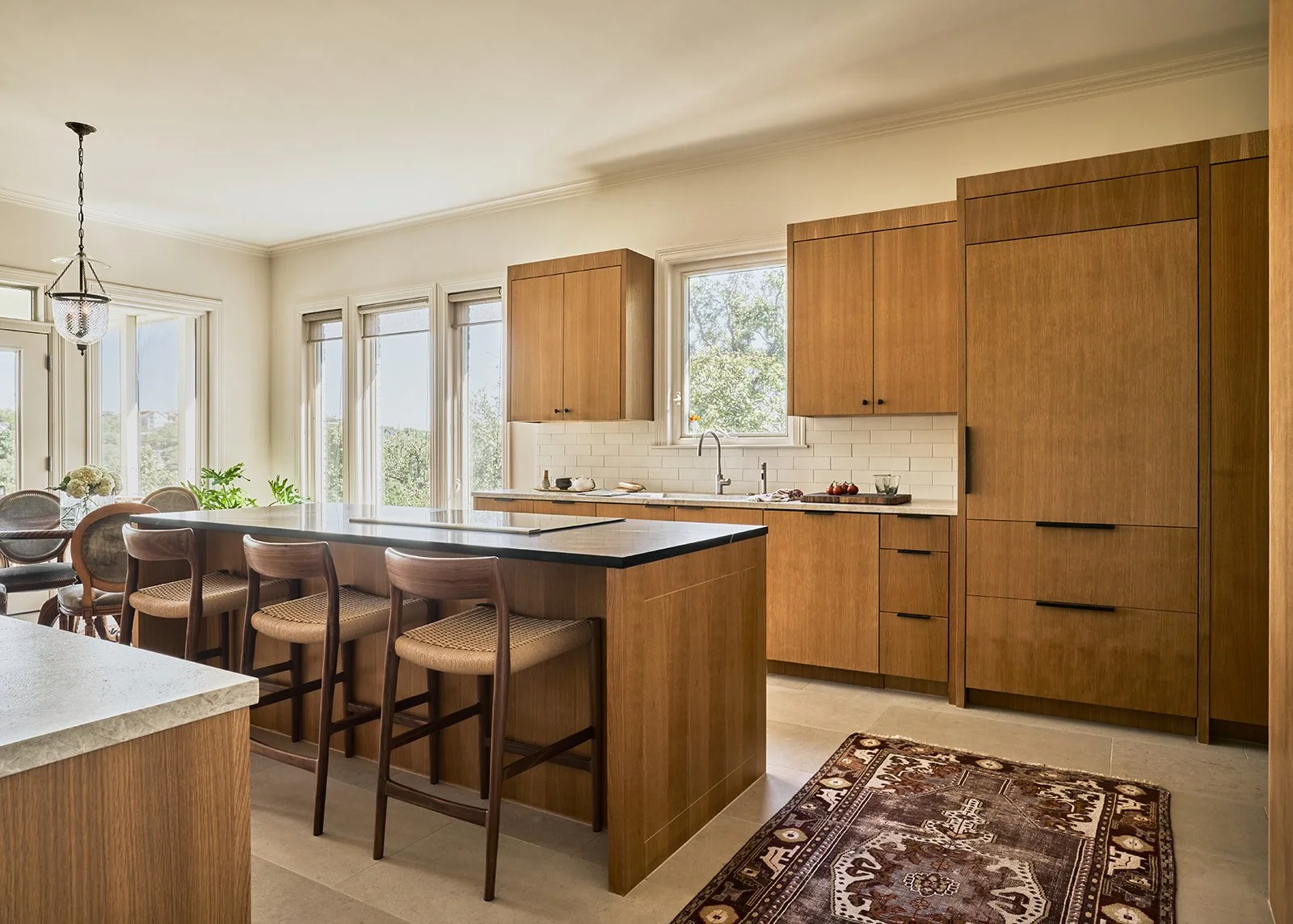 Austin kitchen design blending warm white oak cabinetry with a soapstone island countertop, vintage rug, and mid-century counter stools creating a modern yet inviting space.