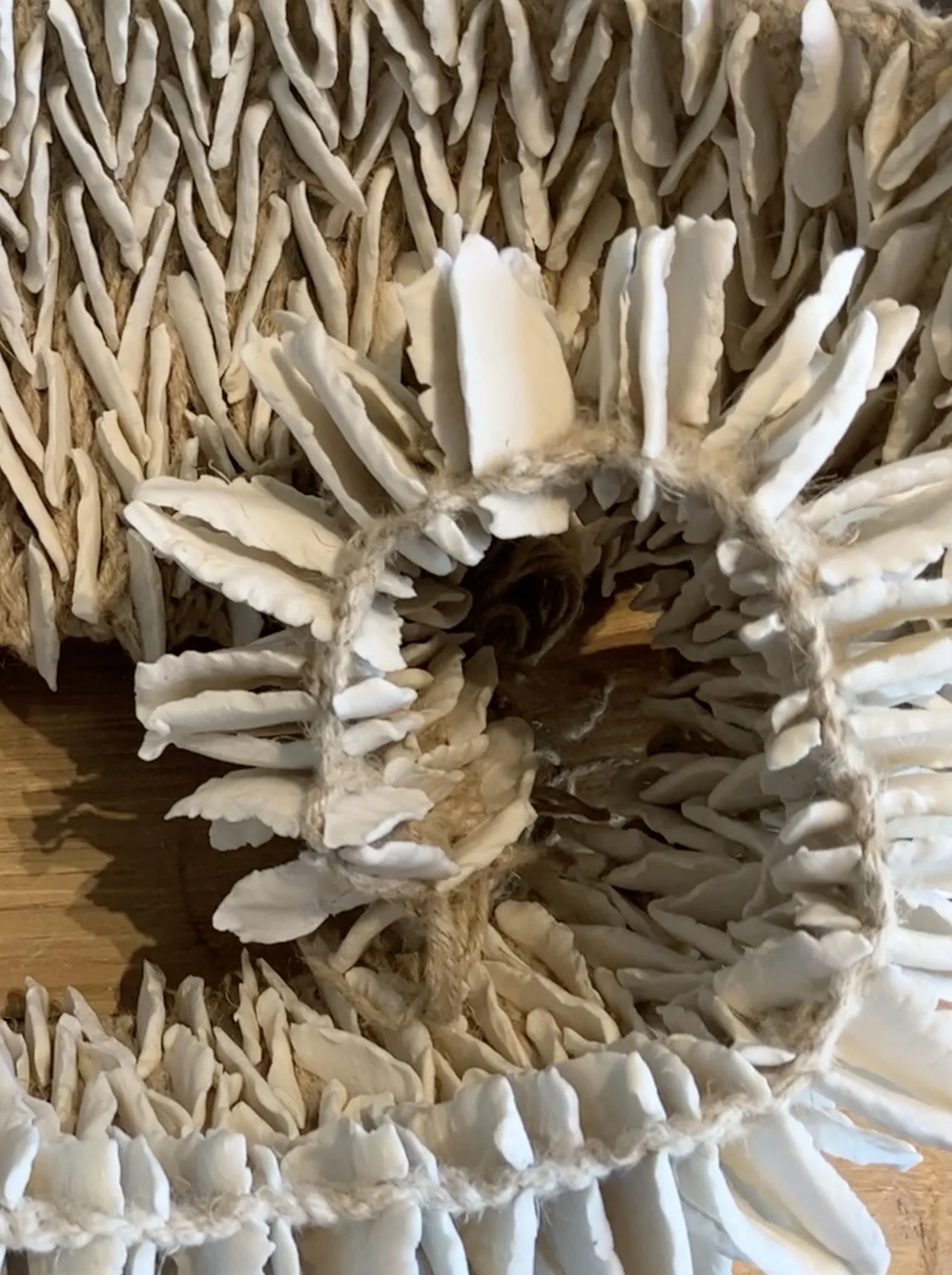 Close-up of the ruffled white porcelain sculpture, showing delicate clay petals stitched in rows onto coiled jute cord.
