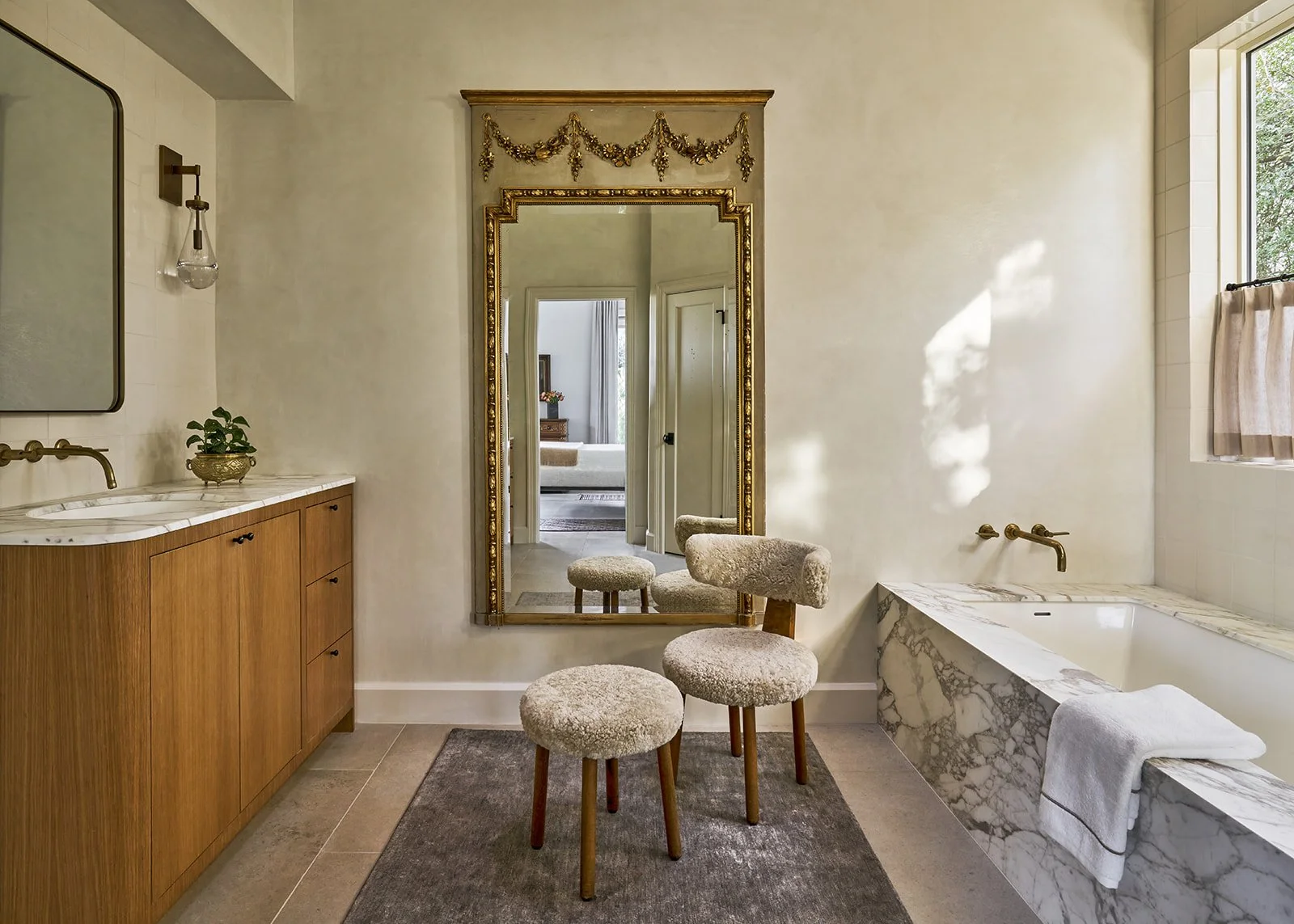 Primary bathroom featuring a marble tub surround, Leuders limestone floors, white oak cabinetry, and an antique Trumeau mirror.
