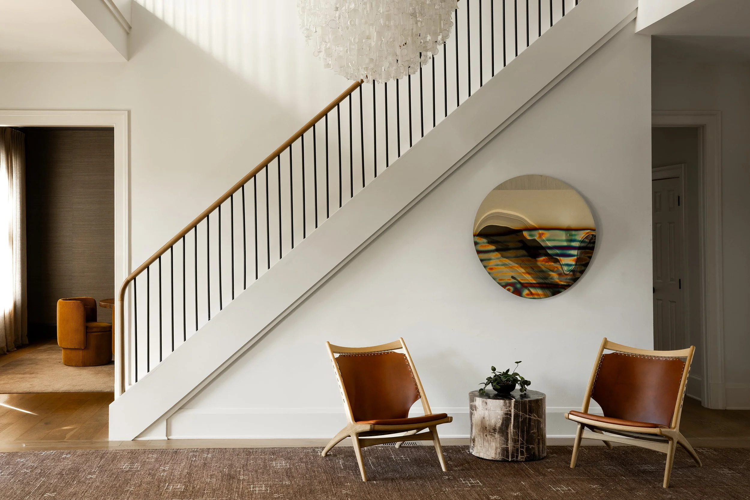 Modern stairwell renovation with a Stuart Haygarth Tide chandelier, an Anton Hendrick Denys mirror, a custom Battilosi rug, and a petrified wood side table.