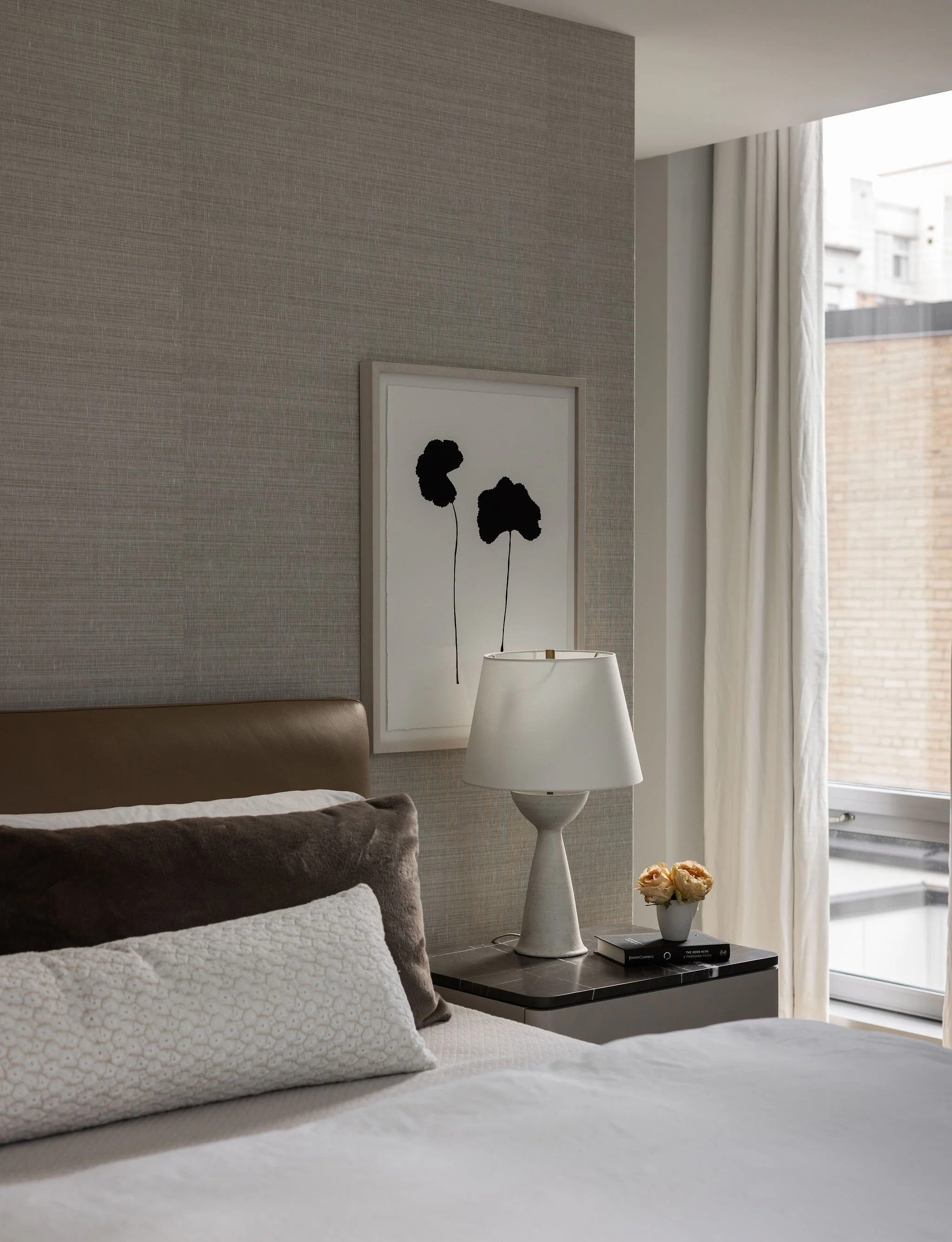 Peaceful primary bedroom in a Georgetown condo, featuring a Minotti bed, plaster table lamp, commissioned Mia Carameros painting, Holly Hunt grasscloth wallpaper, and layered luxury bedding.