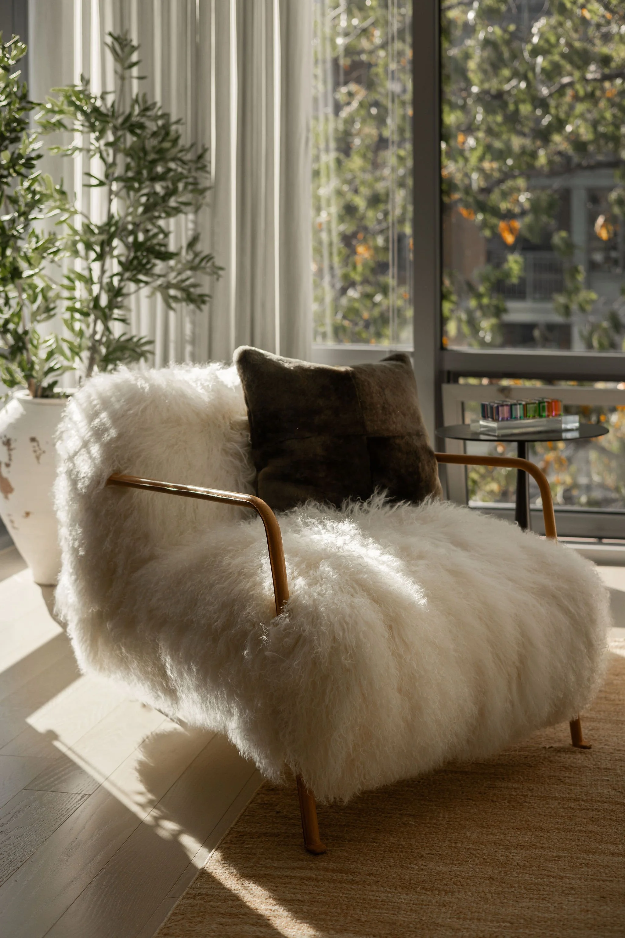Detail of a Bruxelles armchair by Baxter Italy with leather arms, positioned by a large window in a Georgetown condo living room, styled with vintage Vasa Cubes in cast acrylic.