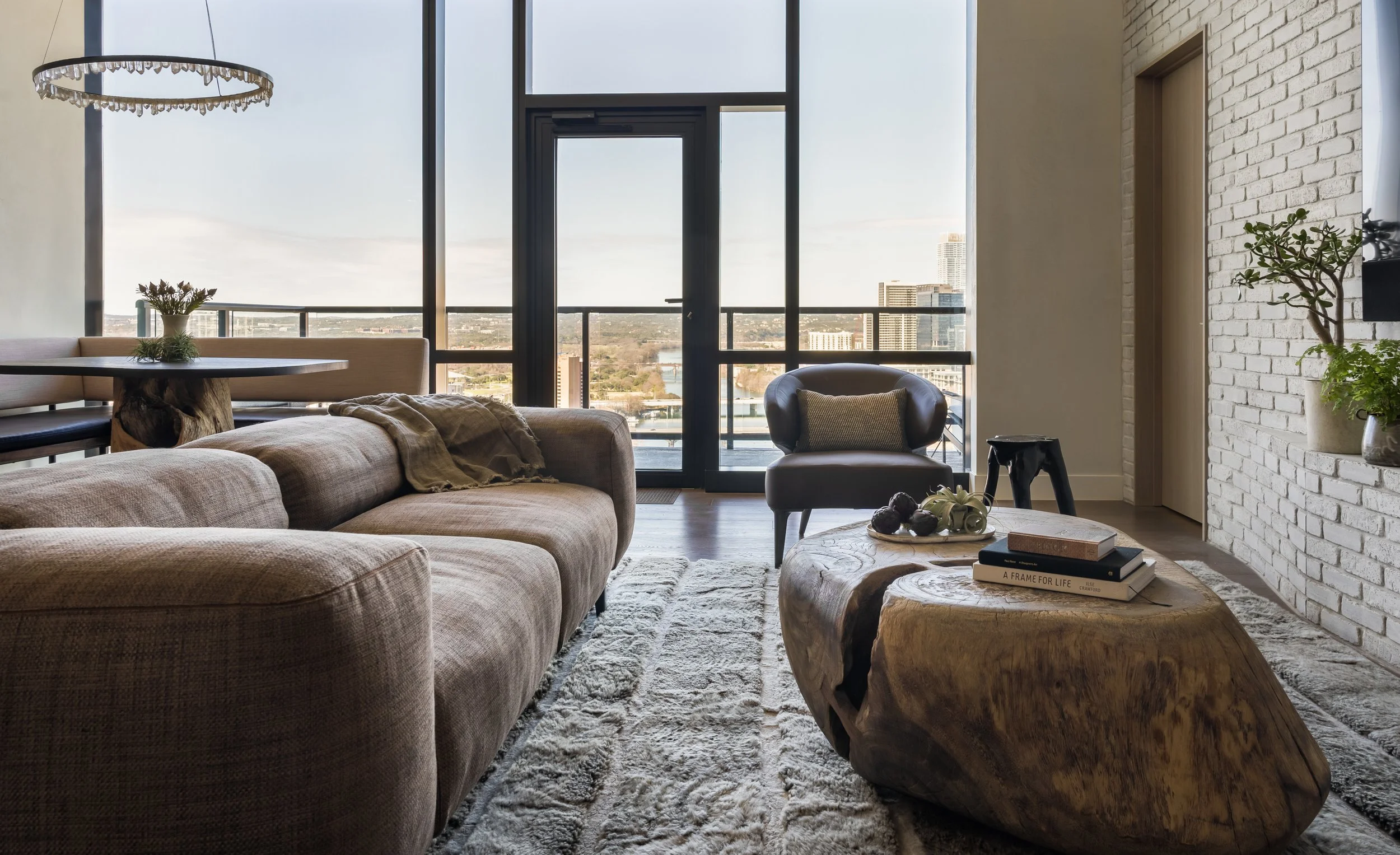 Downtown Austin condo living room with warm, earthy modern furnishings, a sculptural wood coffee table, Minotti leather lounge chair, and expansive urban views.