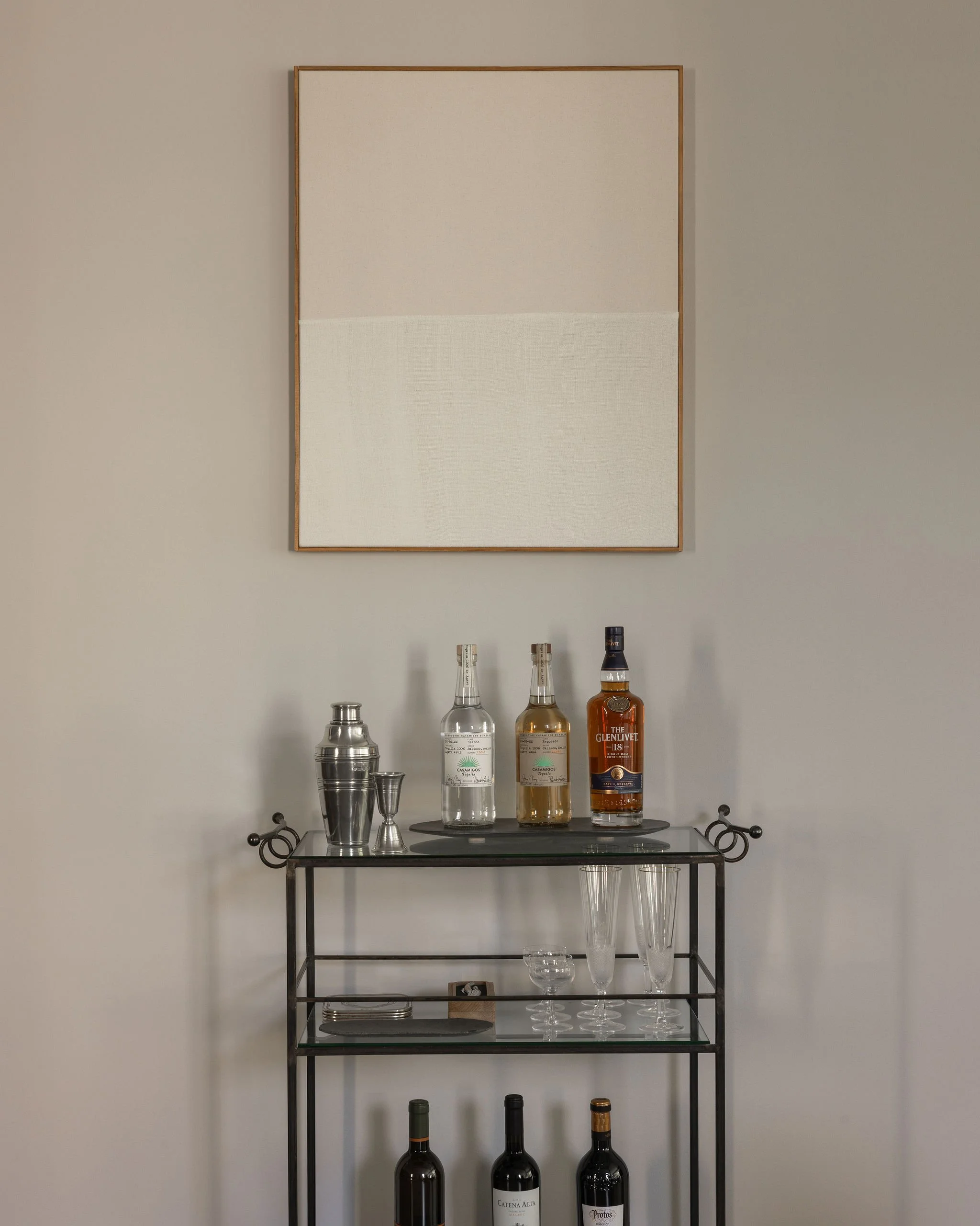 Styled metal and glass bar cart in a Georgetown condo, topped with an abstract textile painting by Ethan Cook and curated barware.