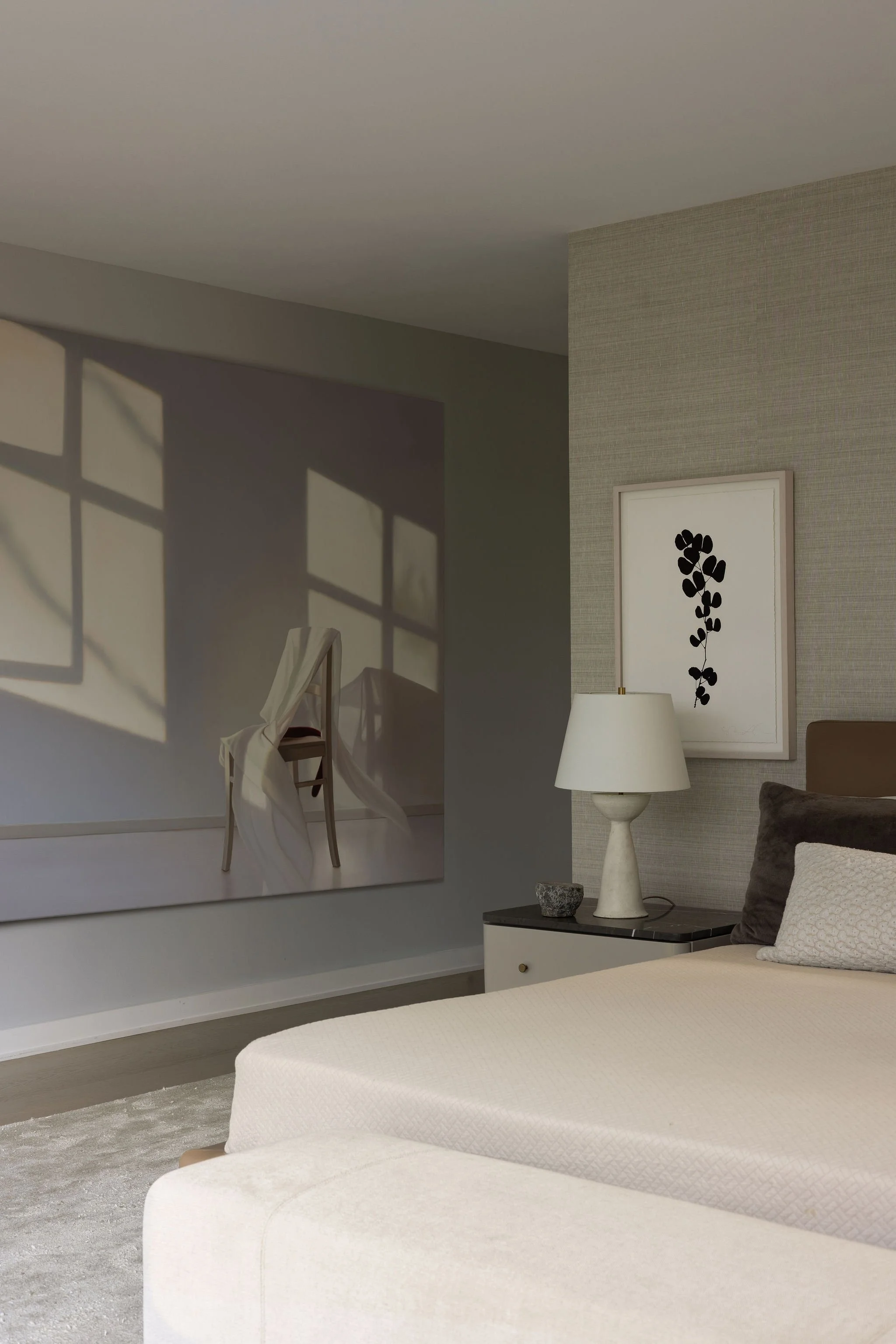 Primary bedroom view with Minotti bed, plaster lamp, grasscloth wallpaper, and an Edite Grinberga painting creating a window-like effect.