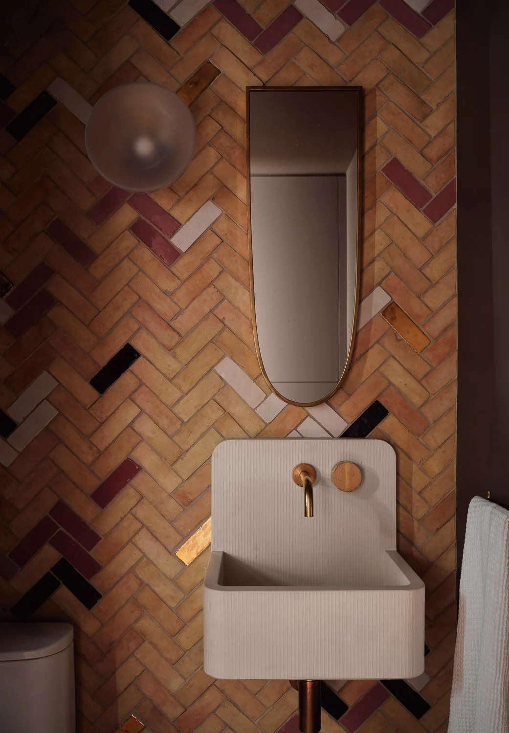 Powder room featuring a herringbone zellige tile feature wall, a wall-hung sink by Kast, and a vintage mirror.