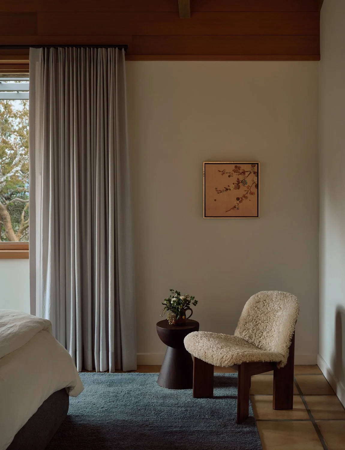 Guest bedroom with a sculptural lounge chair, custom window treatments, and a serene, nature-inspired palette.