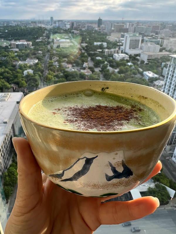 A bowl of matcha held up over a city view