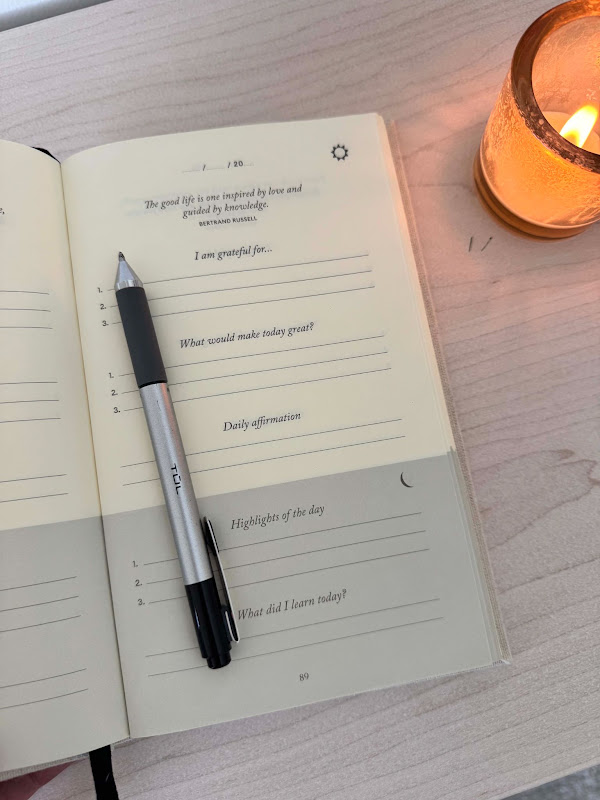 The Five-Minute Journal open to a morning page, a pen and a lit candle beside it